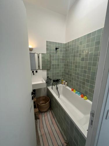 La salle de bains est pourvue d'une baignoire et d'un mur carrelé vert. dans l'établissement Loft familial avec grand jardin verdoyant, à Paris