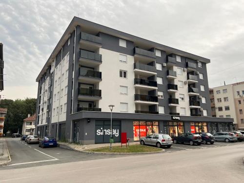 ein großes Gebäude mit auf einem Parkplatz geparkten Autos in der Unterkunft Apartman Max in Modriča