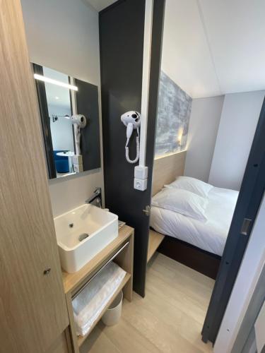 ein Bad mit einem Waschbecken, einem Bett und einem Spiegel in der Unterkunft CAMP'HOTEL in Mamers