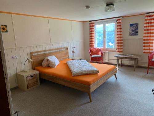 a bedroom with a bed with an orange bedsheet and chairs at Zimmer & z'Morgä Schönenboden in Wildhaus