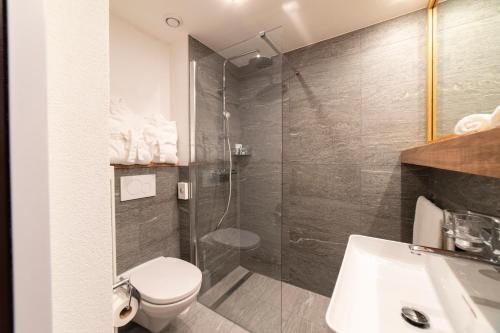 a bathroom with a shower and a toilet and a sink at Hotel Sonne in Wildhaus