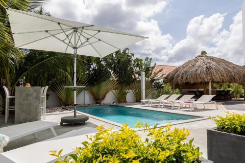 a swimming pool with a white umbrella and lounge chairs and a resort at Tropical Eden Villa in Jan Thiel