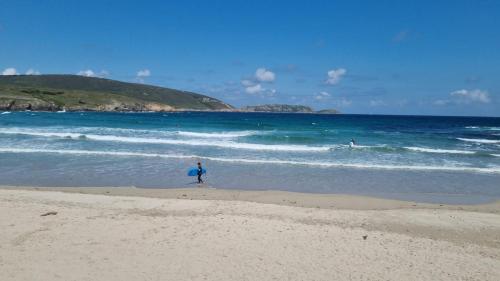a person walking on the beach with a surfboard at Rua as Neves in Malpica
