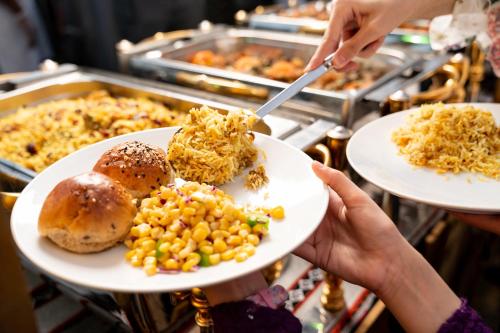a person holding a plate of food with corn and bread at Sheraton Dammam Hotel & Convention Centre in Dammam