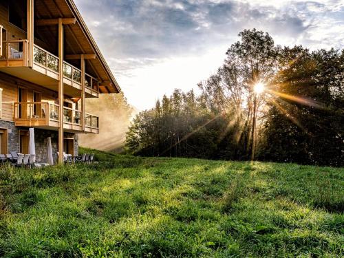 a building with the sun shining on a grass field at Alpine Retreat w Sauna in Abondance
