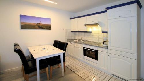 a kitchen with white cabinets and a table with chairs at Gaestehaus-Meene-Menten-Wohnung-MM-2 in Süderhöft