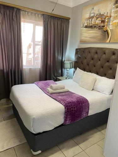 a bedroom with a large bed with a purple blanket at Menlyn Mews Guesthouse in Pretoria
