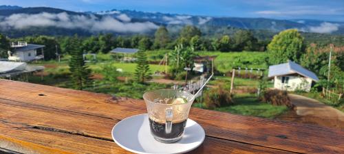 a cup of coffee sitting on top of a wooden table at บ้านไร่ระเบียงฟ้า น้ำหนาว แคมป์ปิ้ง in Ban Phu Hi