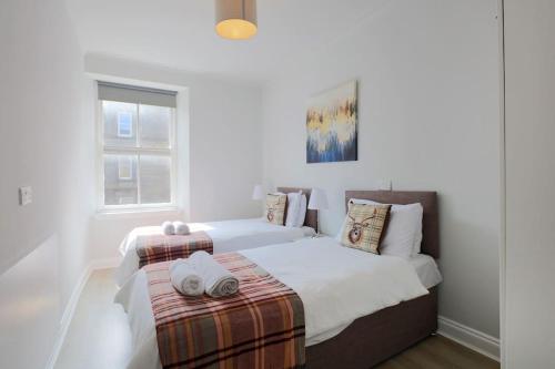 a white bedroom with two beds and a window at Cosy & Central Broughton 2BR Apt near City Centre in Edinburgh