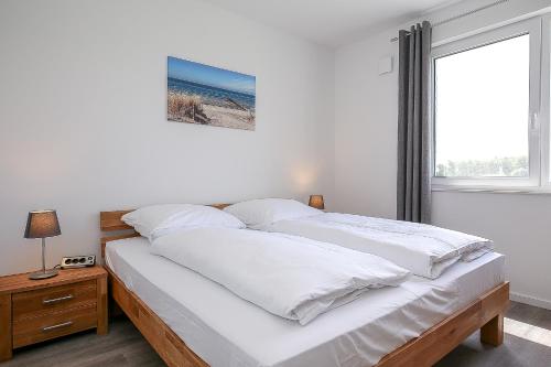 Schlafzimmer mit einem Bett mit weißer Bettwäsche und einem Fenster in der Unterkunft Weiße Villen Wohnung 19 in Boltenhagen