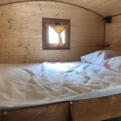 Ce lit se trouve dans une chambre en bois dotée d'une fenêtre. dans l'établissement La roulotte de moulin rouge, à Audelange
