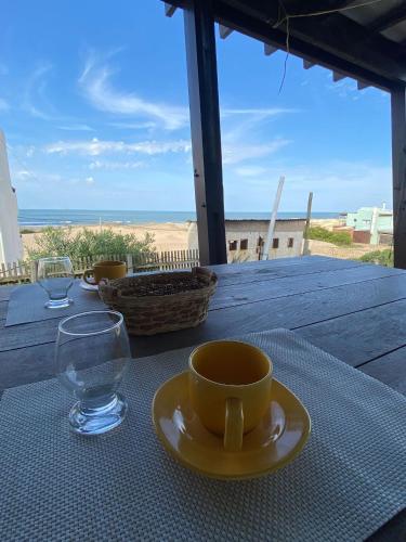 a yellow cup and a glass on a table with the beach at Miralejos in Punta Del Diablo