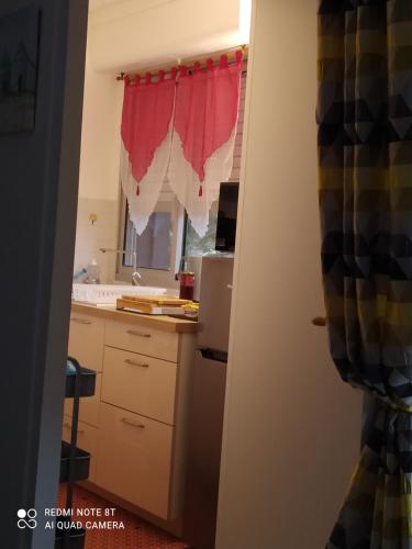 - une cuisine avec des placards blancs et un rideau rouge dans l'établissement Nid douillet proche de la mer et de la gare, à Houlgate