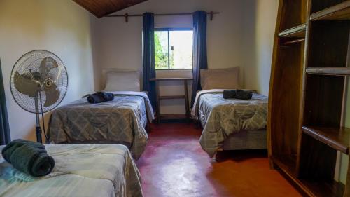 a room with two beds and a fan and a window at Terra Coral - Chapada dos Veadeiros in Alto Paraíso de Goiás