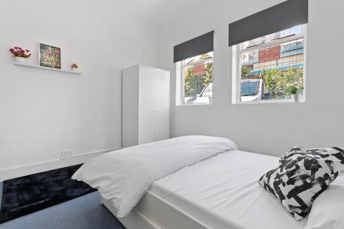 een witte slaapkamer met een bed en 2 ramen bij Fantastic 2BD Barking stay with links to the City! in Londen
