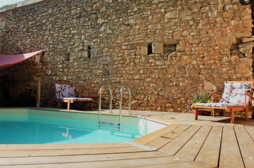 una piscina con 2 sillas junto a una pared de piedra en La Bucolique, Chambres et Jardin d'Hôtes en Sabran
