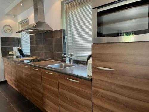 - une cuisine avec des placards en bois et un évier dans l'établissement Ruime en comfortabele bungalow aan bosrand, à Lage Mierde