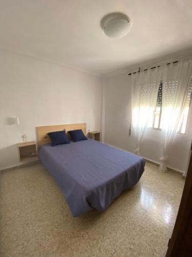 1 dormitorio con cama con sábanas azules y ventana en Piso en la puntilla, en El Puerto de Santa María