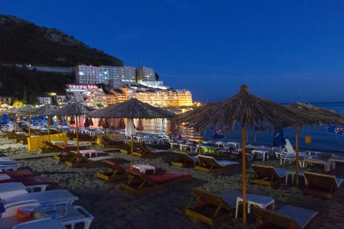 a beach with lounge chairs and umbrellas at night at Hotel Ponta Nova in Budva