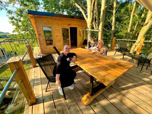 two people sitting at a wooden table on a deck at Zelený ostroff Treehouse in Jiříkov