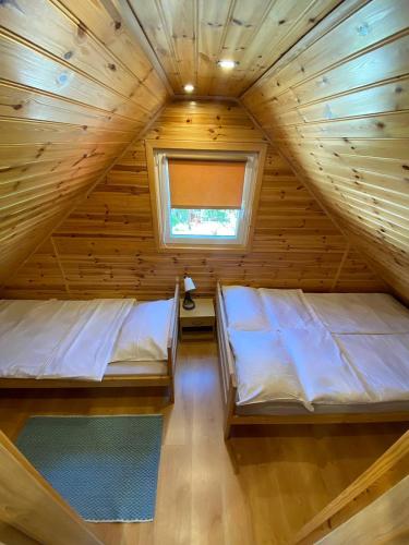 two beds in a wooden room with a window at Domki u Barta in Trzęsacz