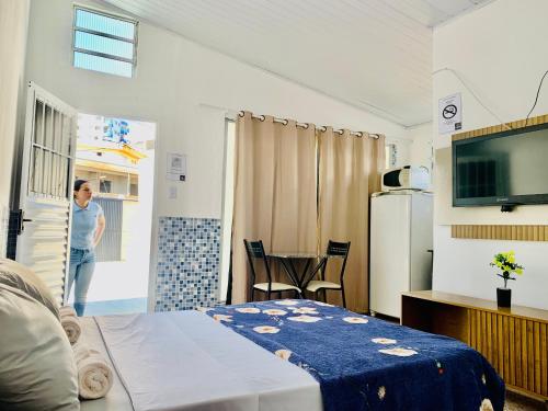a woman is standing in a room with a bedroom at Pousada Aconchego Ocian in Praia Grande