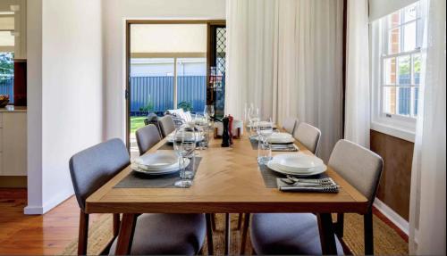 a dining room table with chairs and a long wooden table at Parkview Cottage in Henley Beach South