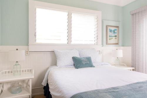 a white bedroom with a white bed with blue pillows at OceanFront Kauai - Harmony TVNC 4247 in Kapaa