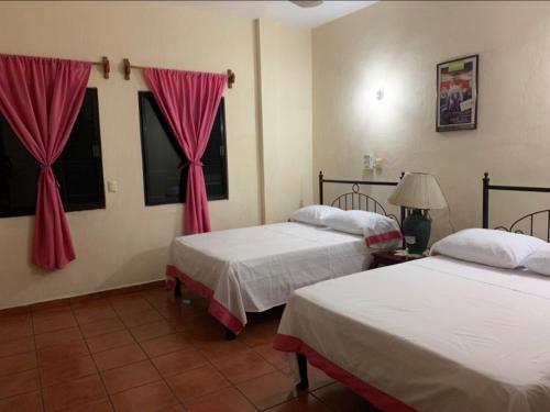 Hotel Jacaranda في توكستلا غوتيريز: سريرين في غرفة مع ستائر وردية