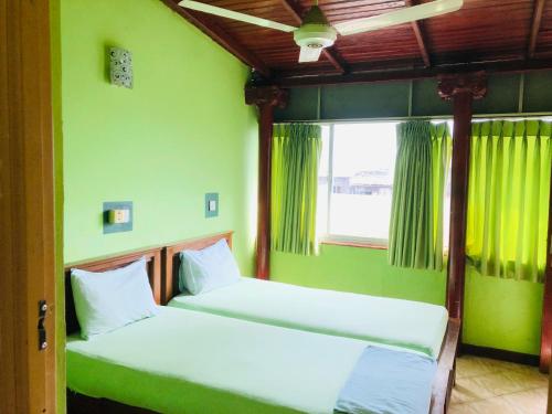 two beds in a room with green walls and a window at Kandyan Holiday Center in Kandy