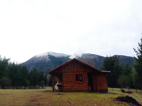 a log cabin in a field with mountains in the background at Cabaña Kiñeco in Melipeuco
