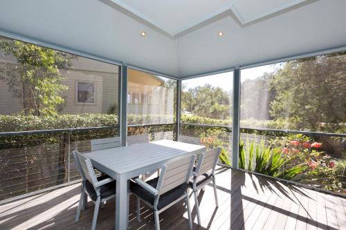 a white table and chairs on a balcony with windows at Blueys Retreat in Blueys Beach