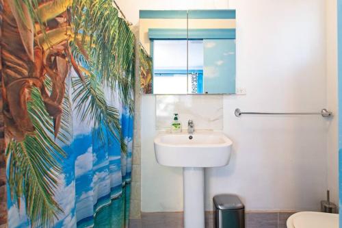 baño con lavabo y un mural de palmeras en Ocean Views Apartment 2 min walk to train & ocean, en Halletts Cove