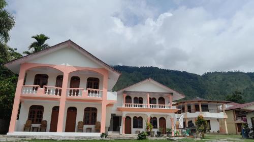 a pink and white house with mountains in the background at Hotel Barbara in Tuktuk Siadong