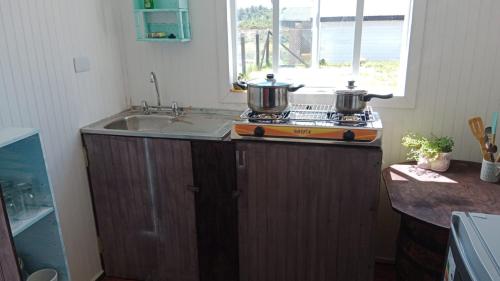 a kitchen with two pots on a stove with a sink at Cabaña y Hospedaje Rural La Familia in Dalcahue
