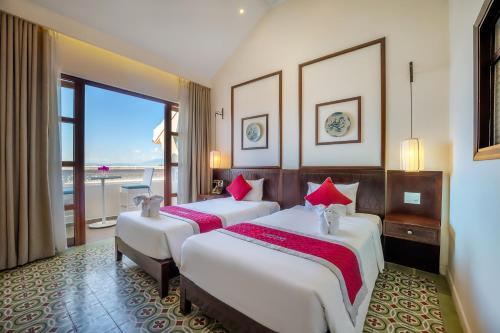 two beds in a hotel room with a large window at Lantana Riverside Hoi An Boutique Hotel & Spa in Hoi An
