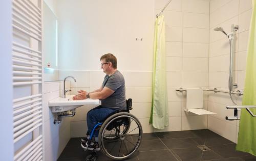 a man in a wheelchair sitting at a sink in a bathroom at WaldResort in Weberstedt