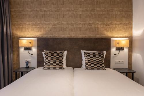two beds in a room with two lamps at Hotel Amsterdam De Roode Leeuw in Amsterdam