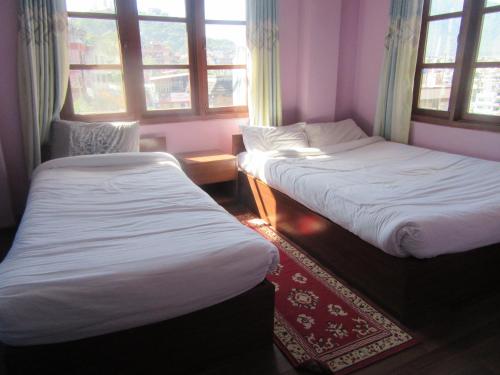 two beds in a room with windows and a rug at STUPA VIEW INN in Kathmandu