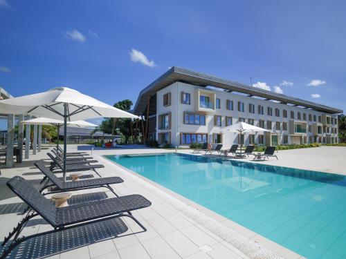 - une piscine avec des chaises et des parasols à côté d'un bâtiment dans l'établissement Ibis Styles Mayotte Aéroport, à Pamandzi