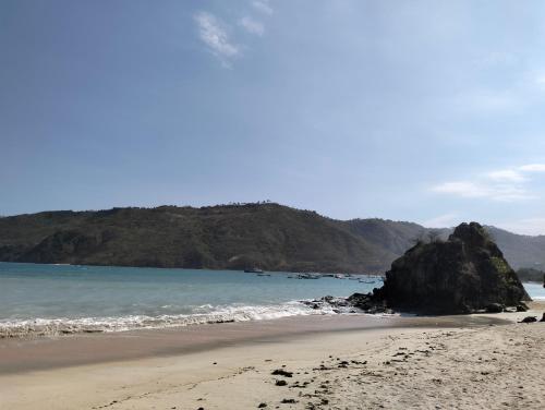 a beach with a large rock in the ocean at T&T Homestay in Kuta Lombok