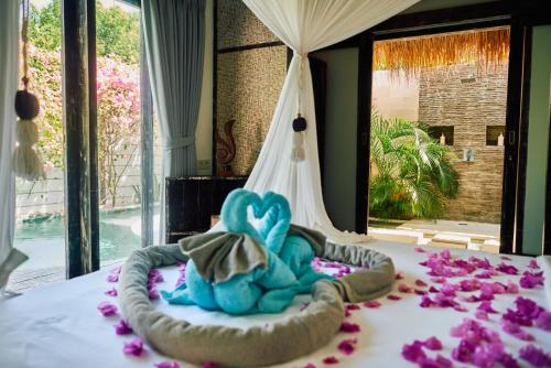 a blue teddy bear on a bed with pink flowers at Atoll Haven Villas in Gili Islands
