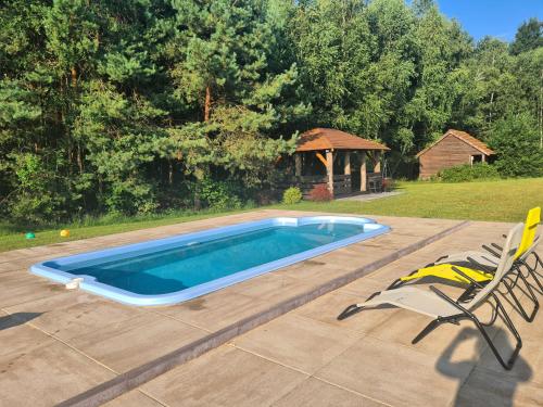 a swimming pool with two chairs and a gazebo at Dworek Ogrodniki, całoroczny dom na wyłączność, basen, sauna, las, staw rybny, altana grillowa, ognisko, pianino, kominek, piec chlebowy, duża ogrodzona posesja in Tuczna