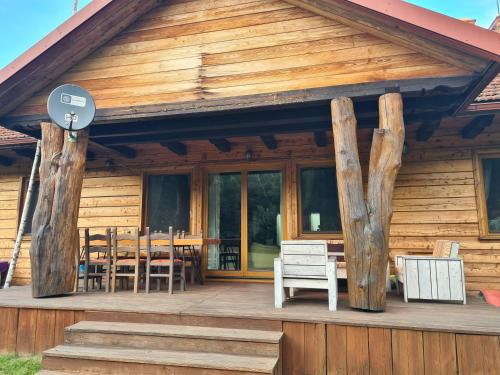 a wooden cabin with a table and chairs on the porch at Dworek Ogrodniki, całoroczny dom na wyłączność, basen, sauna, las, staw rybny, altana grillowa, ognisko, pianino, kominek, piec chlebowy, duża ogrodzona posesja in Tuczna