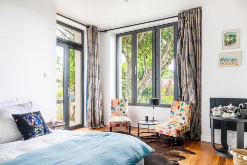 a bedroom with a bed and two chairs and windows at La Villa Lauvray in Vétheuil