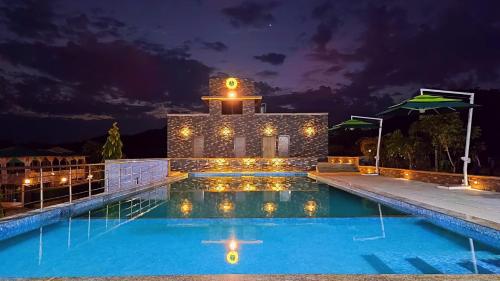 a resort swimming pool at night with a clock tower at The Sky Imperial Nakoda Green Valley Resort in Nāthdwāra