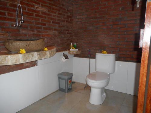 a bathroom with a toilet and a brick wall at Villa Dukuh in Selat
