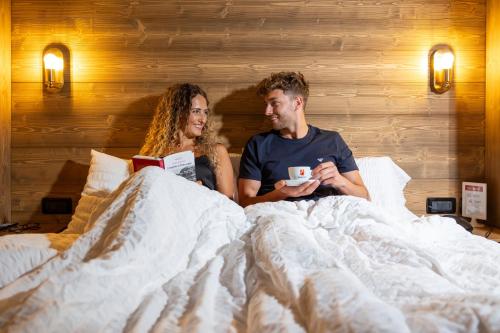 a man and woman sitting in bed reading books at Hotel Derby in Folgarida