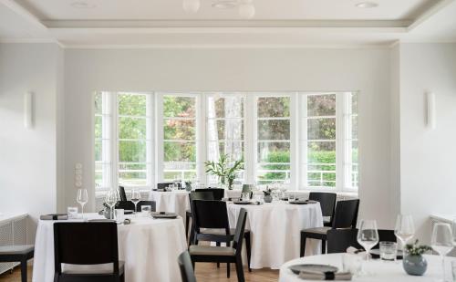 Un comedor con mesas y sillas blancas y ventanas. en Wasa Resort Hotel, Apartments & SPA, en Pärnu