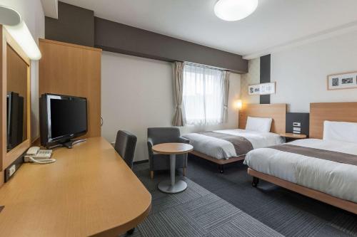 a hotel room with two beds and a desk with a tv at Comfort Hotel Koriyama in Koriyama